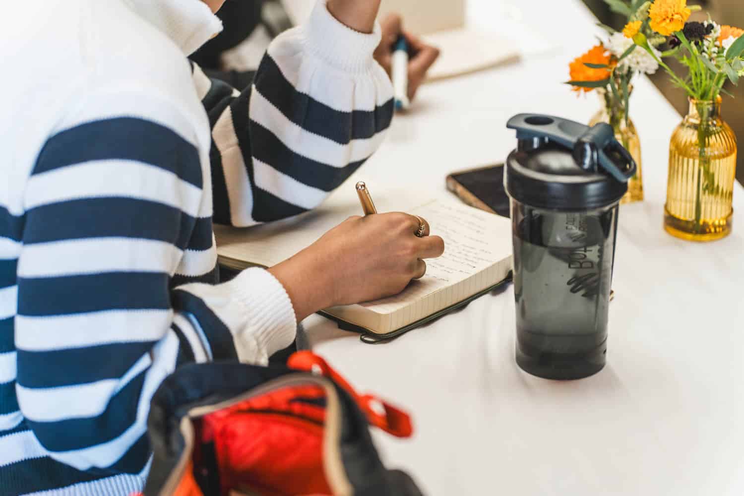 A woman is writing on a notebook while sitting at a table.